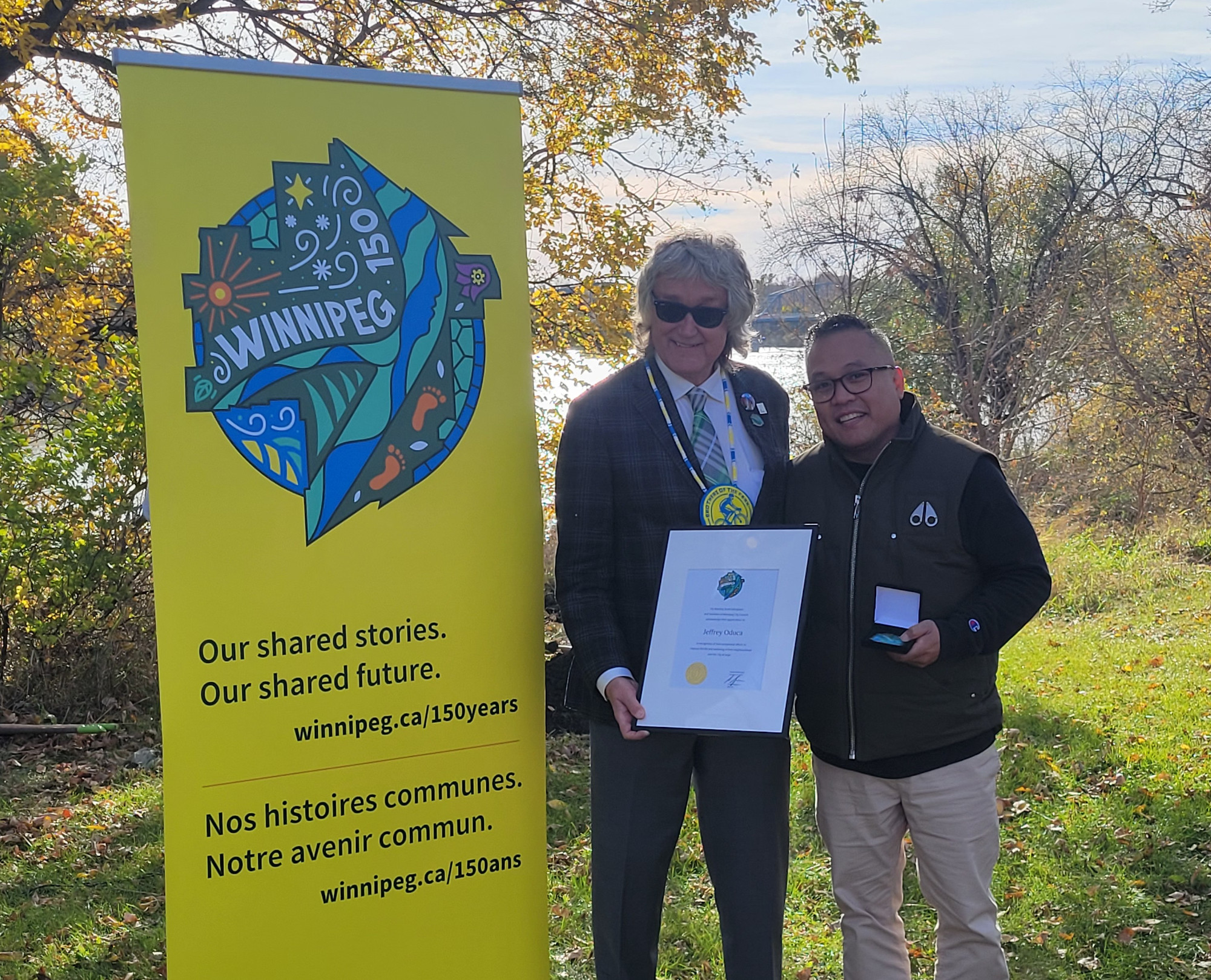 Councillor Ross Eadie presents Jeffrey Oduca with the City of Winnipeg 150th year medal